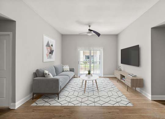 A living room with a grey couch, a white rug, and a ceiling fan.