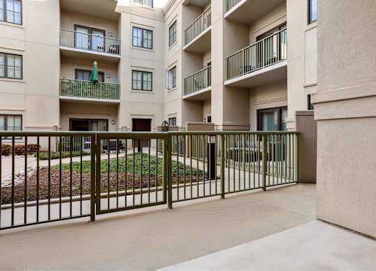 A view of a courtyard with a fence and a building in the background.