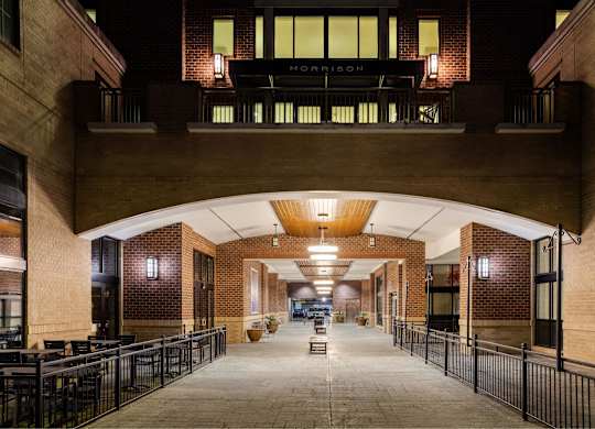 A long hallway with tables and chairs on either side leading to a door at the end.