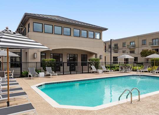 A large swimming pool in front of a building with a striped umbrella.