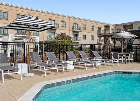 A pool area with sun loungers and umbrellas in front of a building.