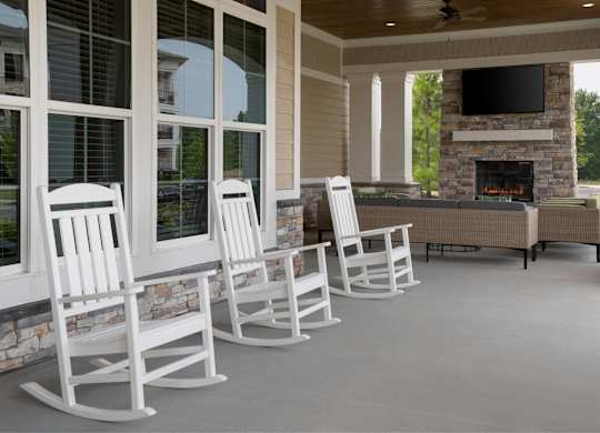 A row of white rocking chairs are lined up in front of a fireplace.