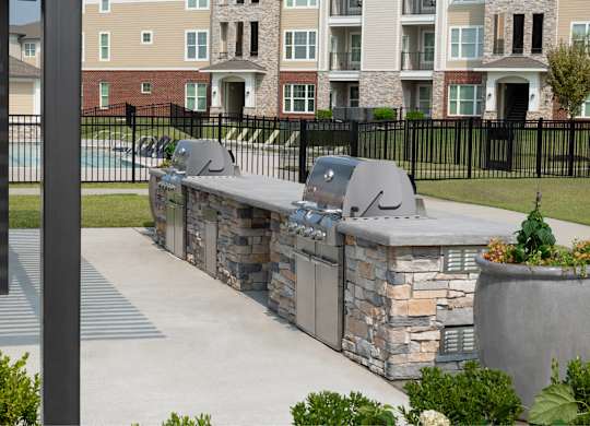 A stone barbecue grill is in the middle of a concrete patio.