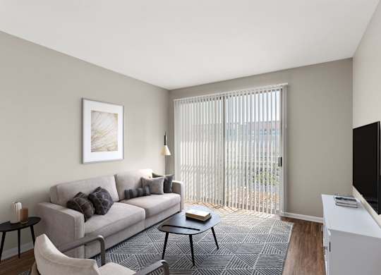 A living room with a grey couch, a black chair, a small table, a television, and a window with blinds.