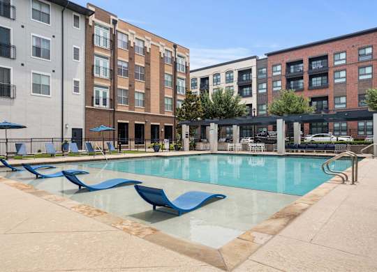 A pool surrounded by chairs and buildings.
