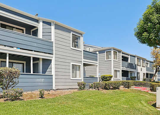 A row of grey and blue houses with green lawns in front.