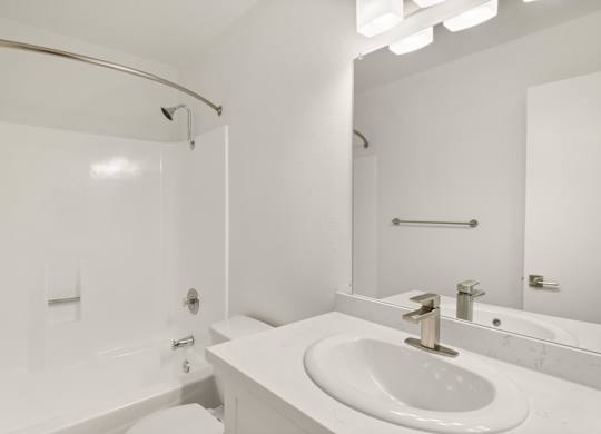 A white bathroom with a sink, mirror, and bathtub.