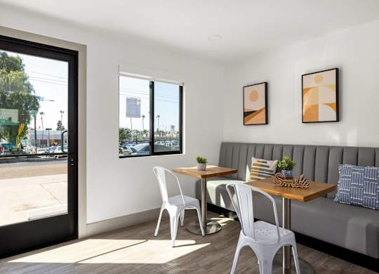 A white chair is in front of a grey couch with a table and two chairs in between.
