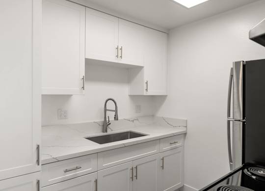 A kitchen with white cabinets and a black refrigerator.