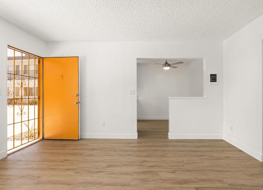 A room with a wooden floor and white walls, with a ceiling fan and a door leading to a balcony.