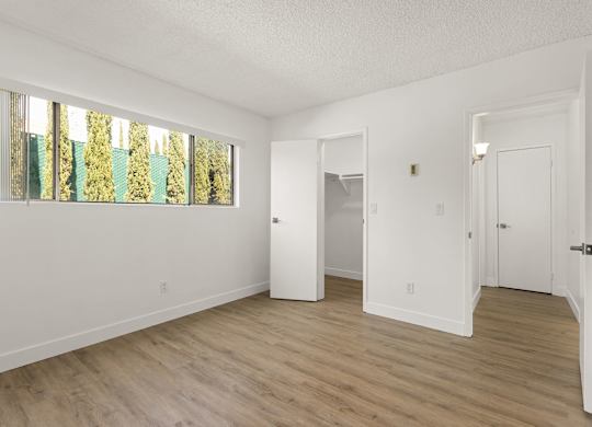 A white room with wood floors and a large window.