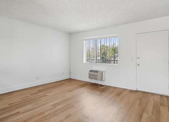 A room with wooden floors and white walls, a window with blinds, and a white door.