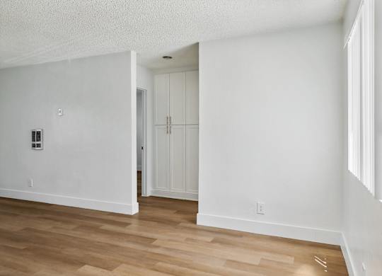 A room with white walls and wooden flooring with a doorway leading to another room.