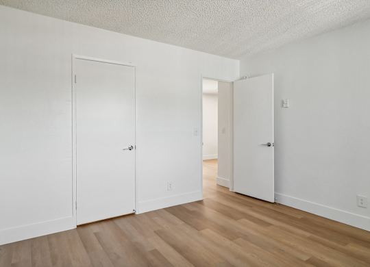A room with white walls and wooden flooring with two doors.