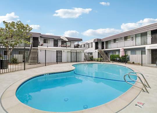 A swimming pool in front of a building with a black fence around it.