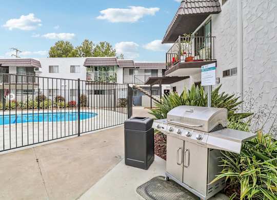 A BBQ grill and trash bin are on a patio next to a pool.
