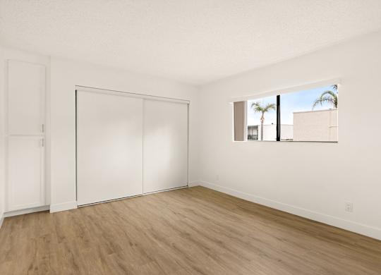 A room with white walls and wood flooring with a large window.