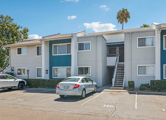 A car is parked in front of a two-story apartment building.