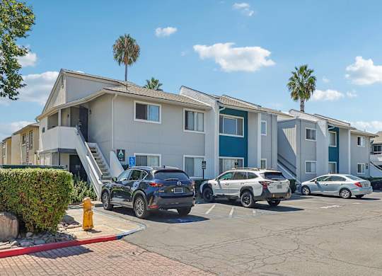 A parking lot with cars and a building with palm trees in the background.