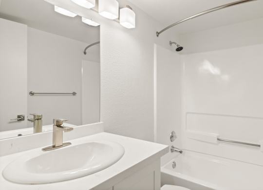 A white bathroom with a sink, mirror, and shower.