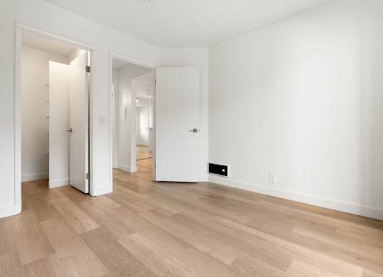 A room with white walls and wooden flooring with two open doors.