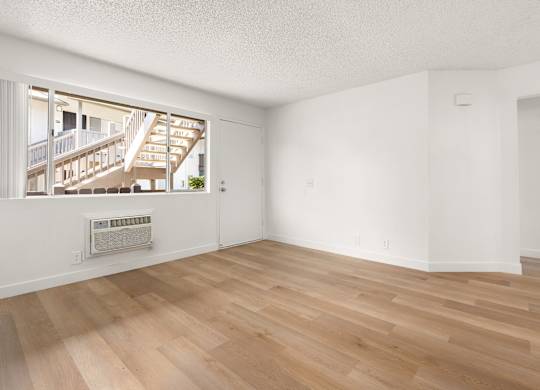 A room with wooden flooring and a window overlooking a balcony.
