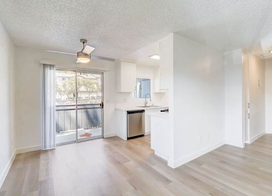 A spacious, empty room with a kitchenette and sliding glass doors leading to a balcony.
