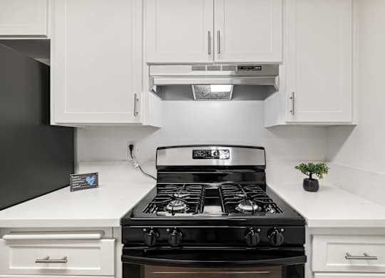A black stove top oven with four burners and a silver range hood above it.