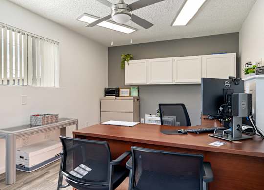 A room with a desk, chairs, and a ceiling fan.