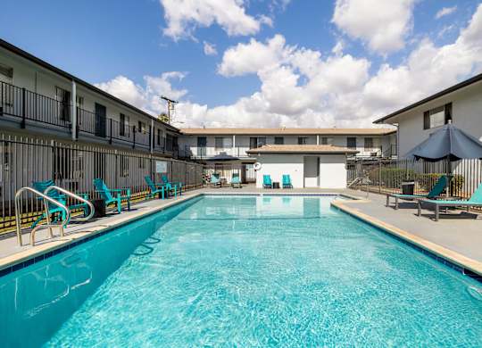 A large swimming pool in front of a building with lounge chairs and umbrellas.