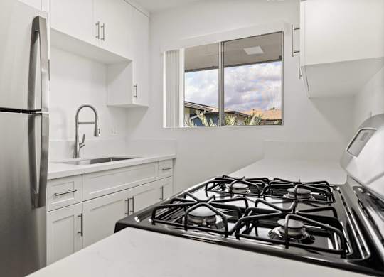 A modern kitchen with a stainless steel refrigerator, a stove, and white cabinets.