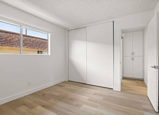 A room with white walls and wooden flooring with a window.