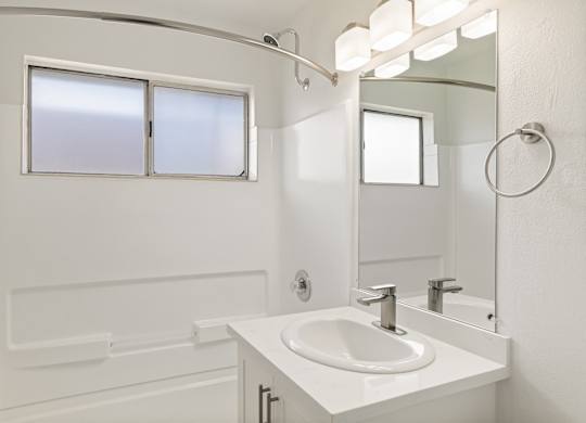 A white bathroom with a sink, mirror, and tub.