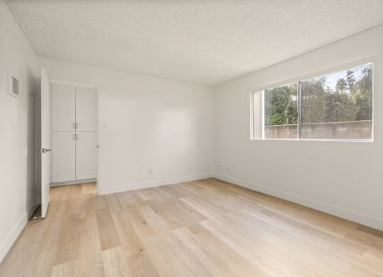 A room with wooden flooring and a window overlooking a fence.