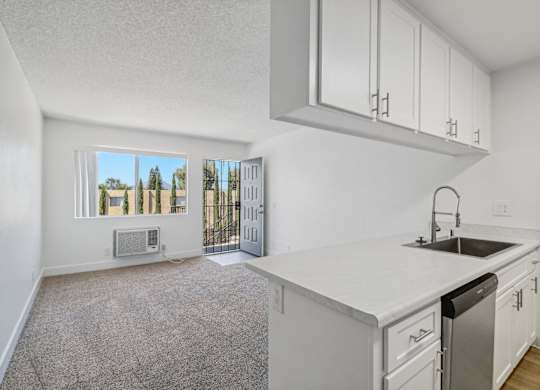 A kitchen with white cabinets and a white countertop with a sink and dishwasher.