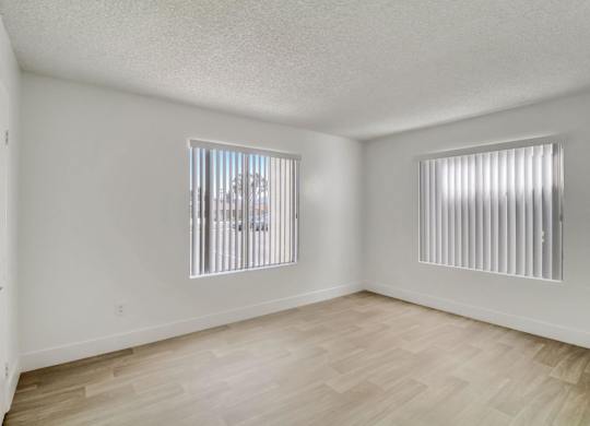 A room with wooden flooring and two windows with blinds.