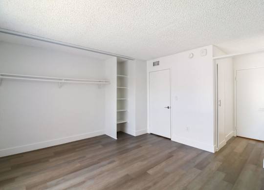 A room with white walls and wooden flooring with a closet and a door.