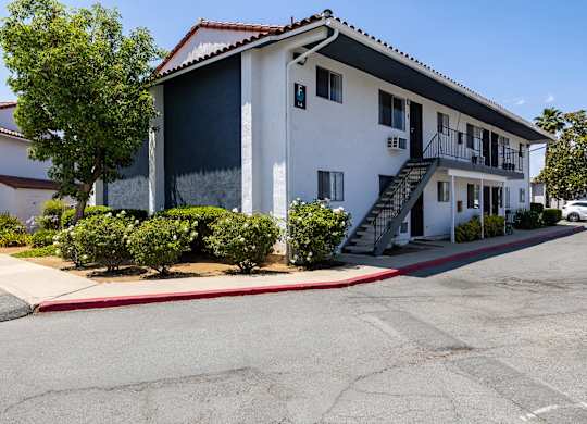 A white building with a red tile roof and a parking lot in front.