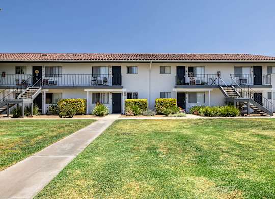 A white building with a red tile roof and a green lawn in front.