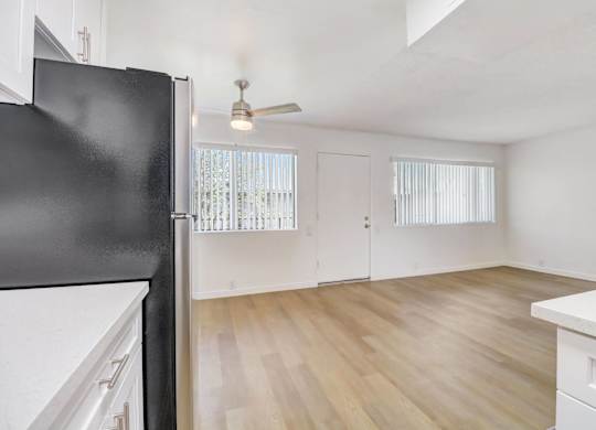 A black fridge in a kitchen with white cabinets and a wooden floor.