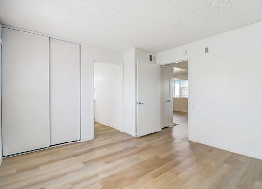 A room with white walls and wooden flooring with a white door and a white wardrobe.