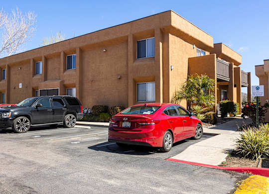 A red car is parked in front of a tan building.