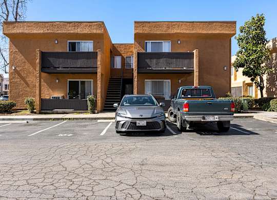 Two cars are parked in a cracked parking lot in front of a tan apartment building.