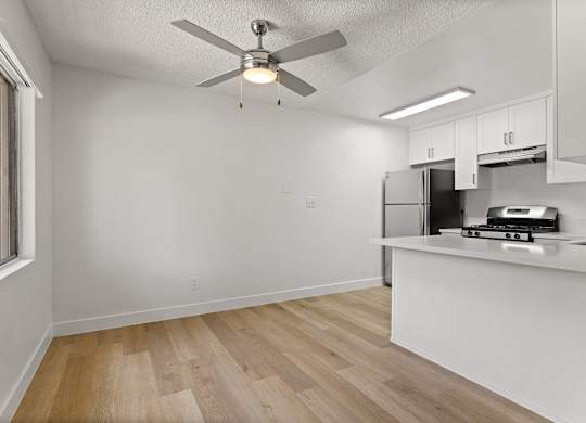 A kitchen with a white ceiling fan and wooden floors.