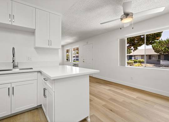 A kitchen with white cabinets and a window overlooking a backyard.