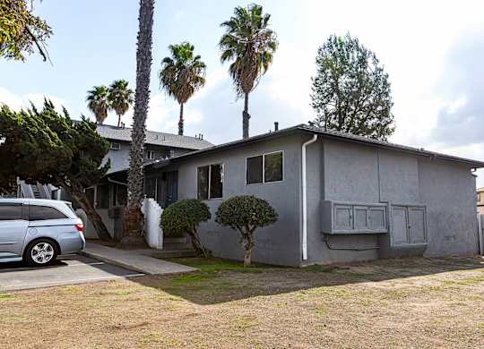A house with a grey exterior is surrounded by trees and a car is parked in front.