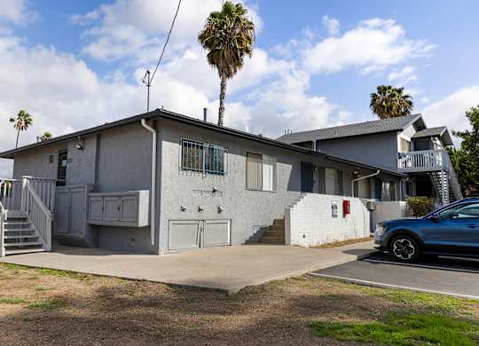 A blue car is parked in front of a house with a palm tree in the background.