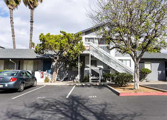 A car is parked in a parking lot in front of a building with a tree.