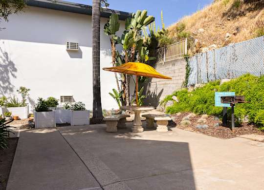 A patio area with a yellow umbrella and a white building in the background.
