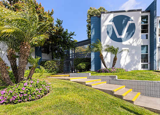 A building with a logo on it is surrounded by a green lawn and trees.